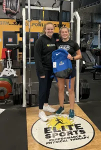 Maggie McCready is holding field hockey equipment at Elite Sports Performance & Physical Therapy 