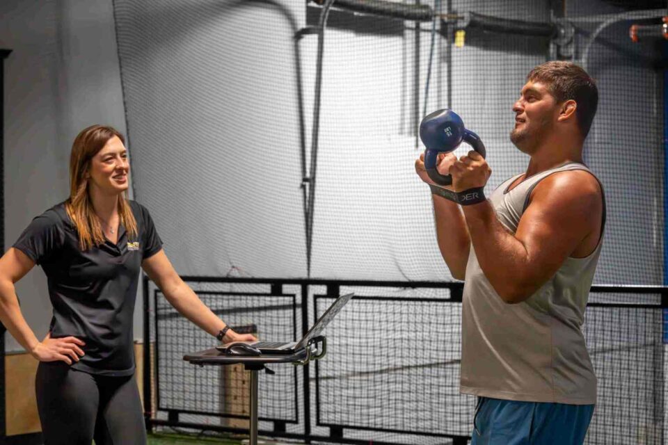 Man lifting kettlebell with trainer at Elite Sports Performance & Physical Therapy