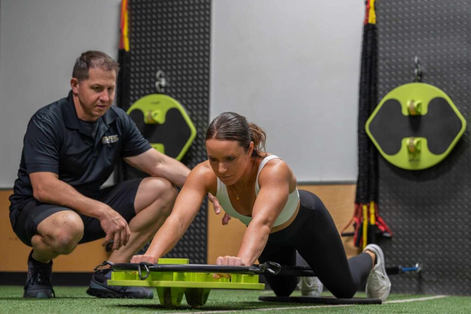 Trainer guiding woman using a lime green core trainer in Foxboro, MA