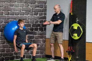 Trainer guiding boy doing wall squats with a resistance band in Foxboro, MA