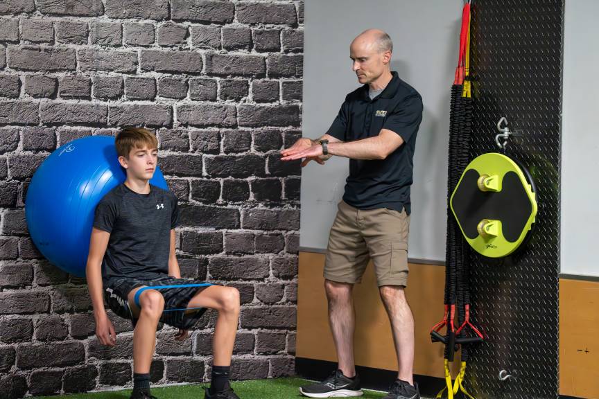 Trainer guiding boy doing wall squats with a resistance band in Foxboro, MA