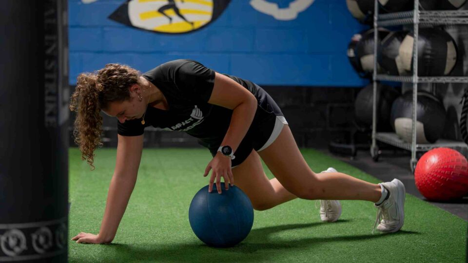 Woman doing plank on a blue medicine ball in a gym in Foxboro, MA